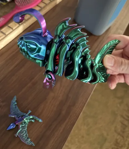Articulated skeleton anglerfish 3D print in green and blue color-shift filament held in a hand